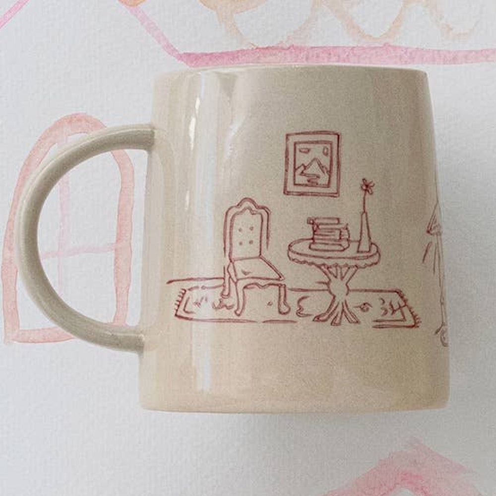Cream ceramic mug with a red hand-stamped illustration of a cozy room scene.