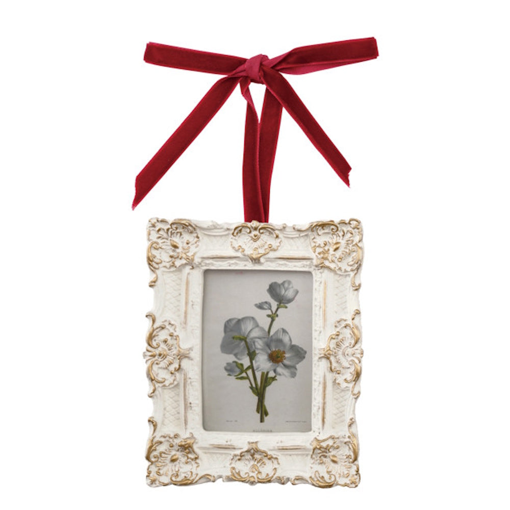 Ornate white and gold picture frame ornament with a red velvet ribbon bow and floral illustration.