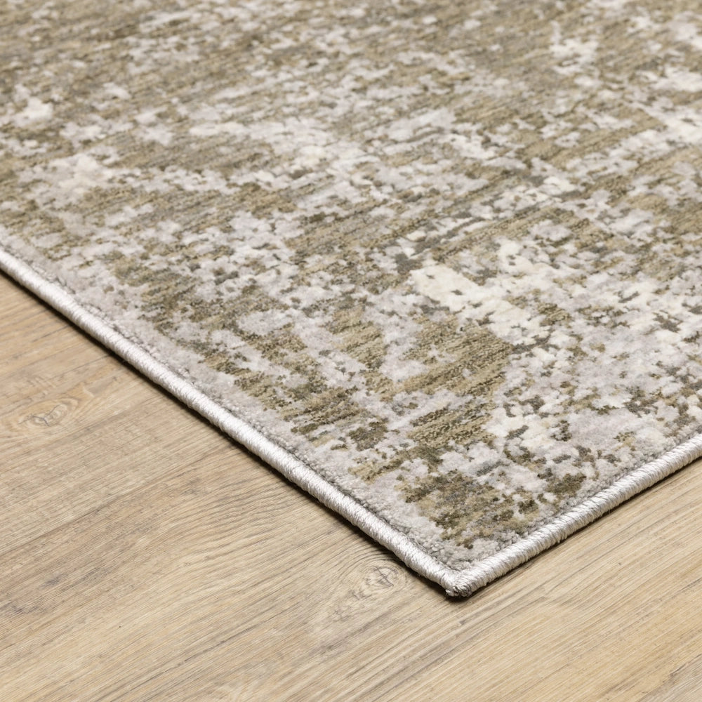 Close-up corner view of the abstract gray, taupe, and cream distressed area rug resting on a wooden floor.