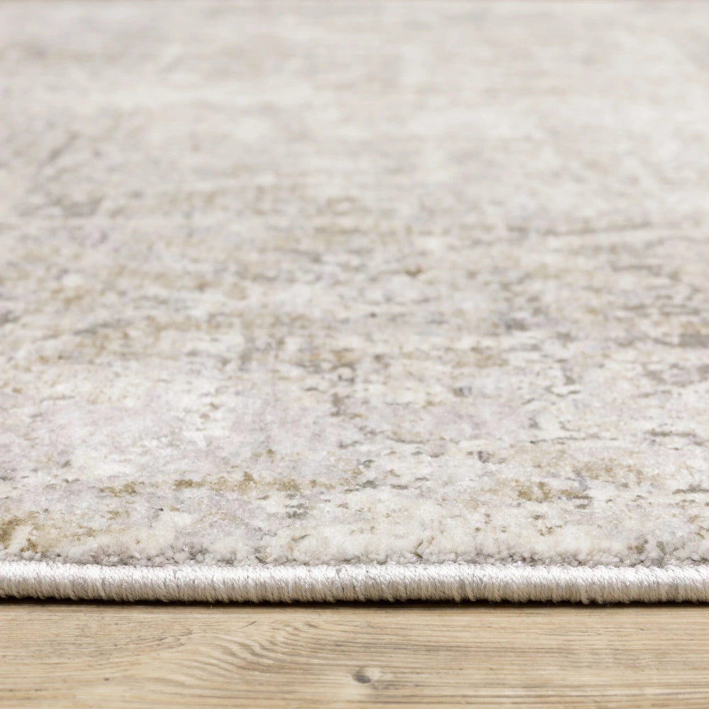 Low-angle view of the abstract gray, taupe, and cream distressed area rug showing its texture and bound edge on a wooden floor.