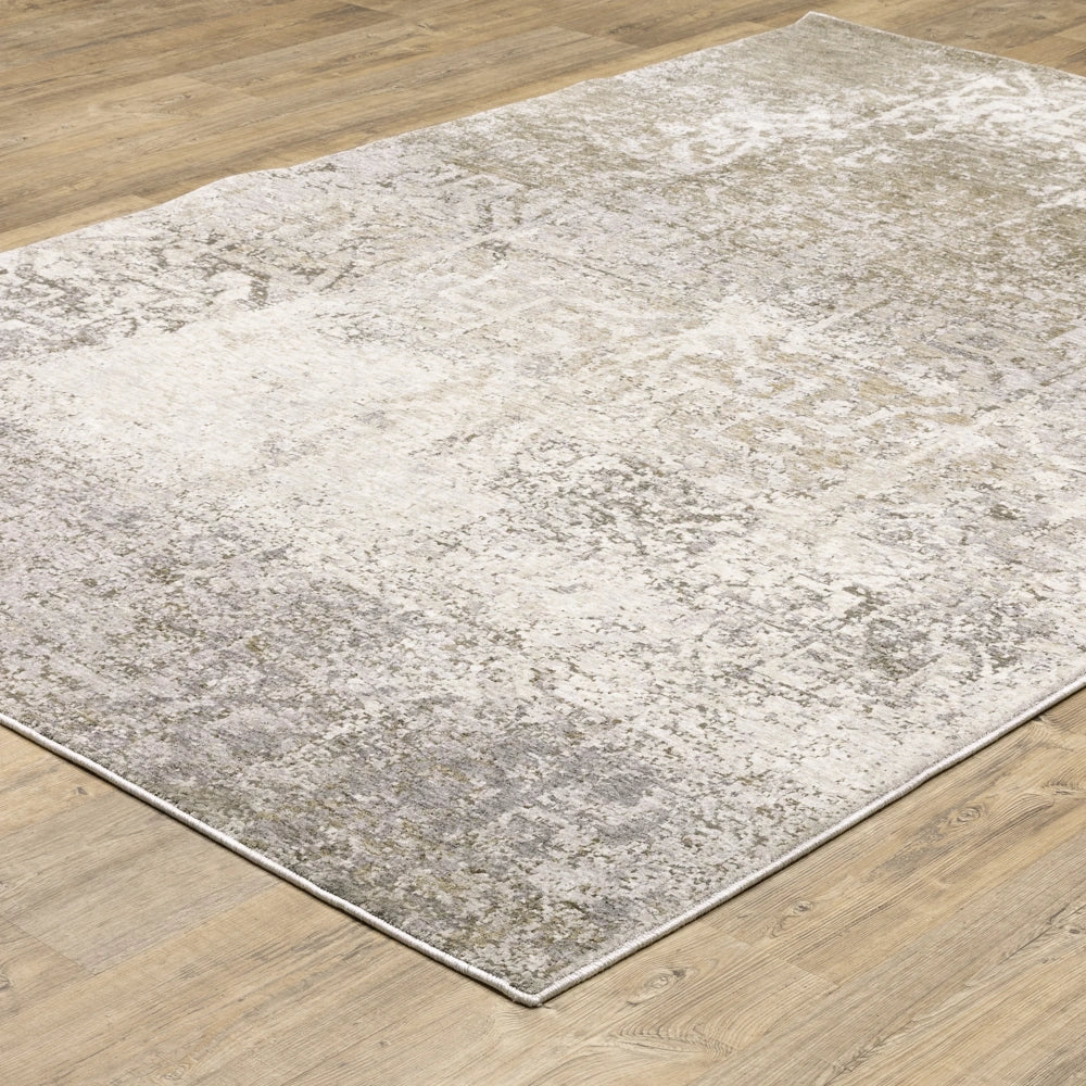 Angle view of the abstract gray, taupe, and cream distressed area rug laid out on a light wood floor.