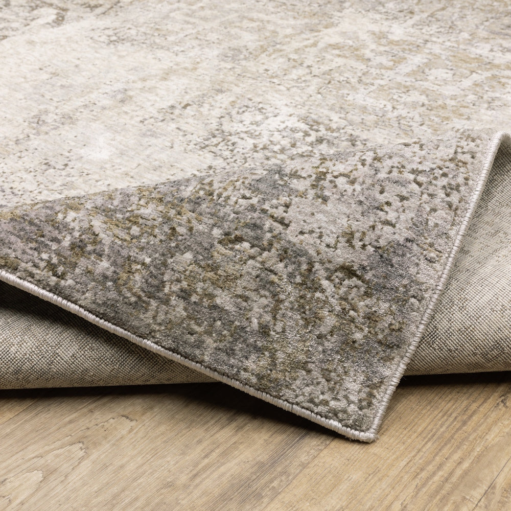 Corner of the gray, taupe, and cream area rug folded to show its finished binding edge and backing on a wooden floor.