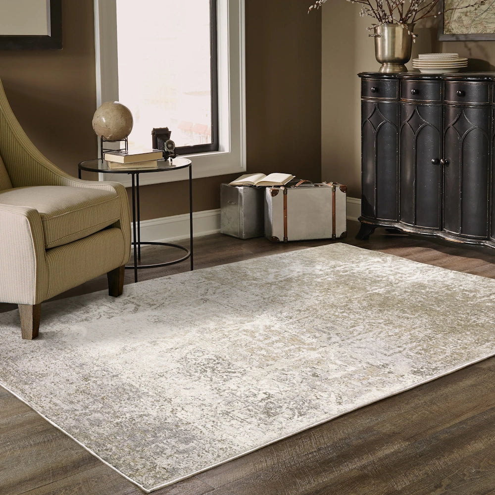 Lifestyle view of the gray, taupe, and cream area rug in a living room with an armchair, side table, and dark cabinet.