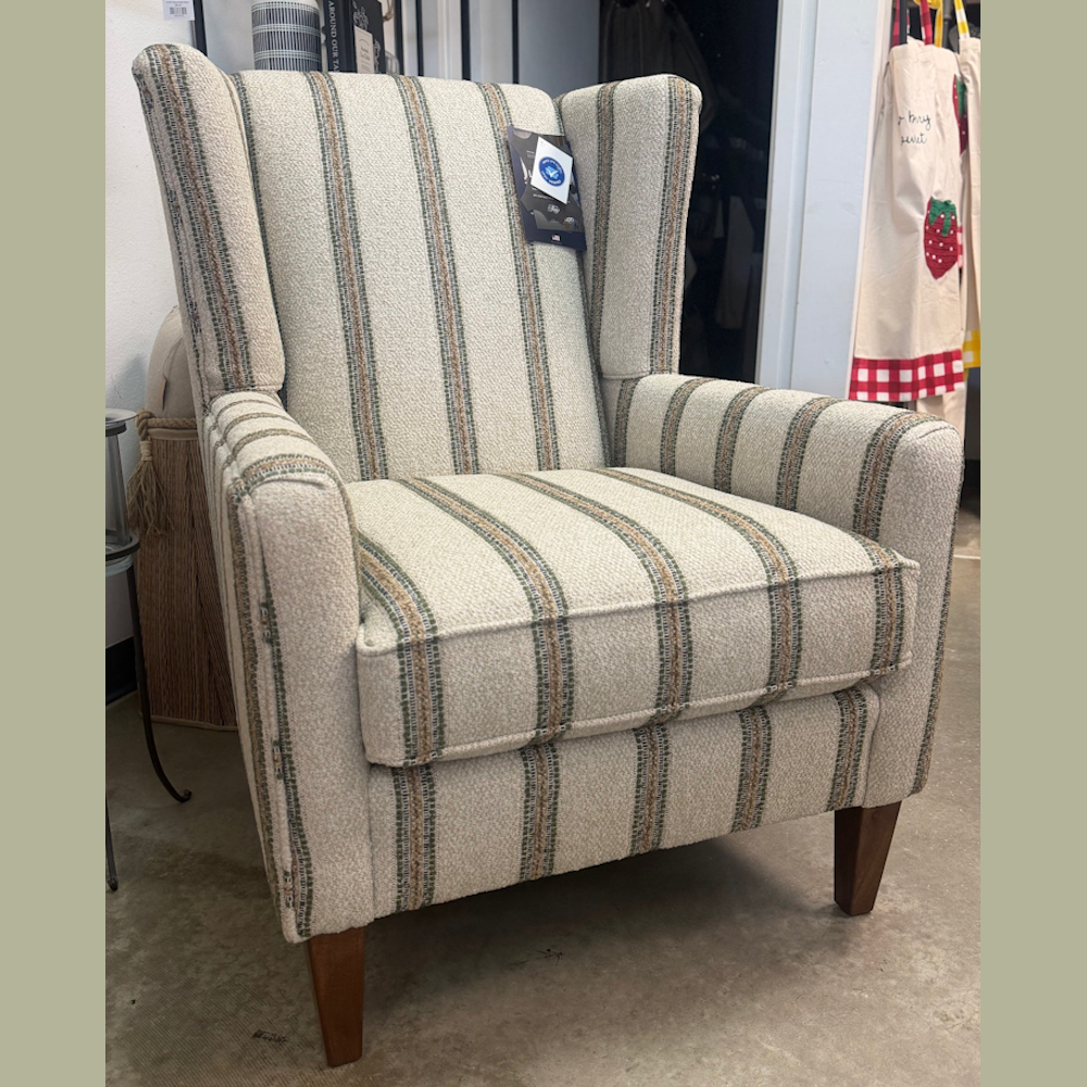 Mid-century modern wingback armchair with striped tweed upholstery and a price tag, sitting on a concrete floor in a furniture store.