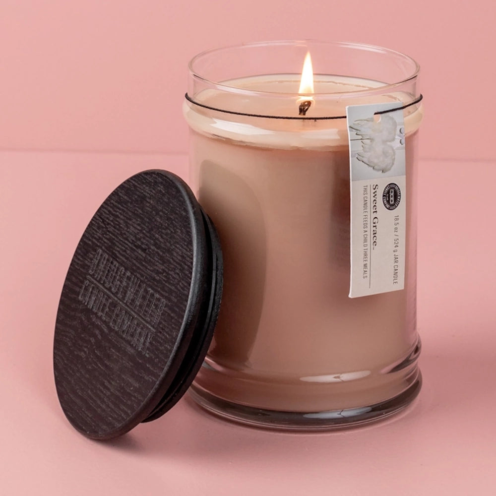 Lit glass jar candle with blush pink wax and a dark wooden lid against a dusty pink background.