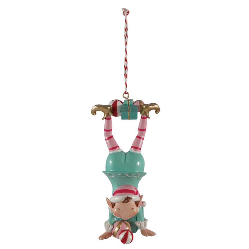 Whimsical Christmas elf hanging upside down while balancing gifts on its feet and hands.