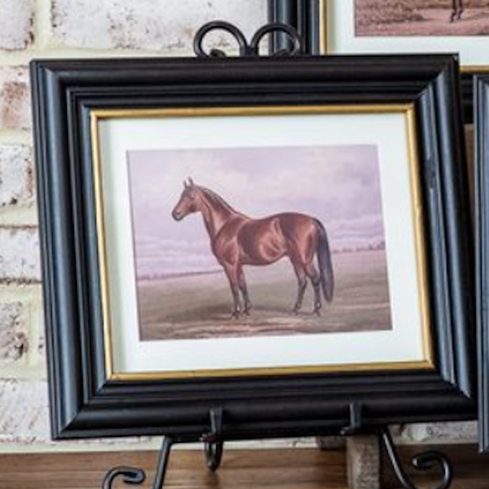 Framed brown horse art print in a black frame with gold trim, displayed on a metal easel.