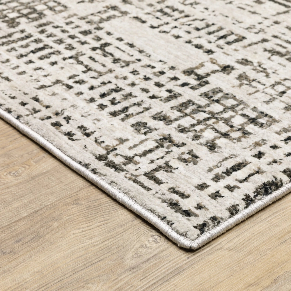 Close-up corner view of the abstract gray and cream patterned area rug resting on a wooden floor.