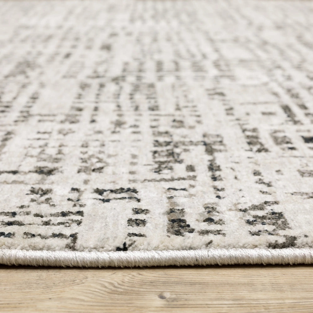 Low-angle view of the gray and cream area rug showing its texture and bound edge on a wooden floor.