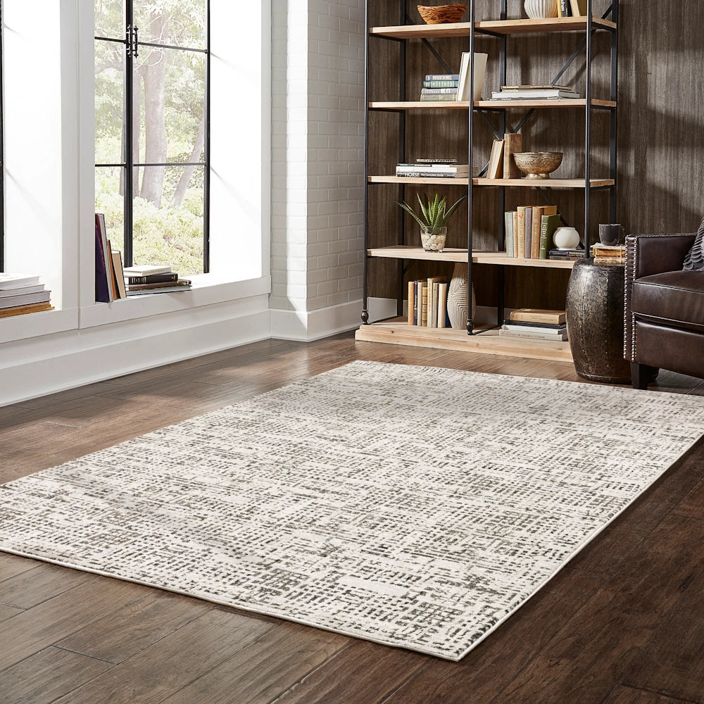 Lifestyle view of the gray and cream area rug in a living room with a large window, bookshelf, and leather chair.