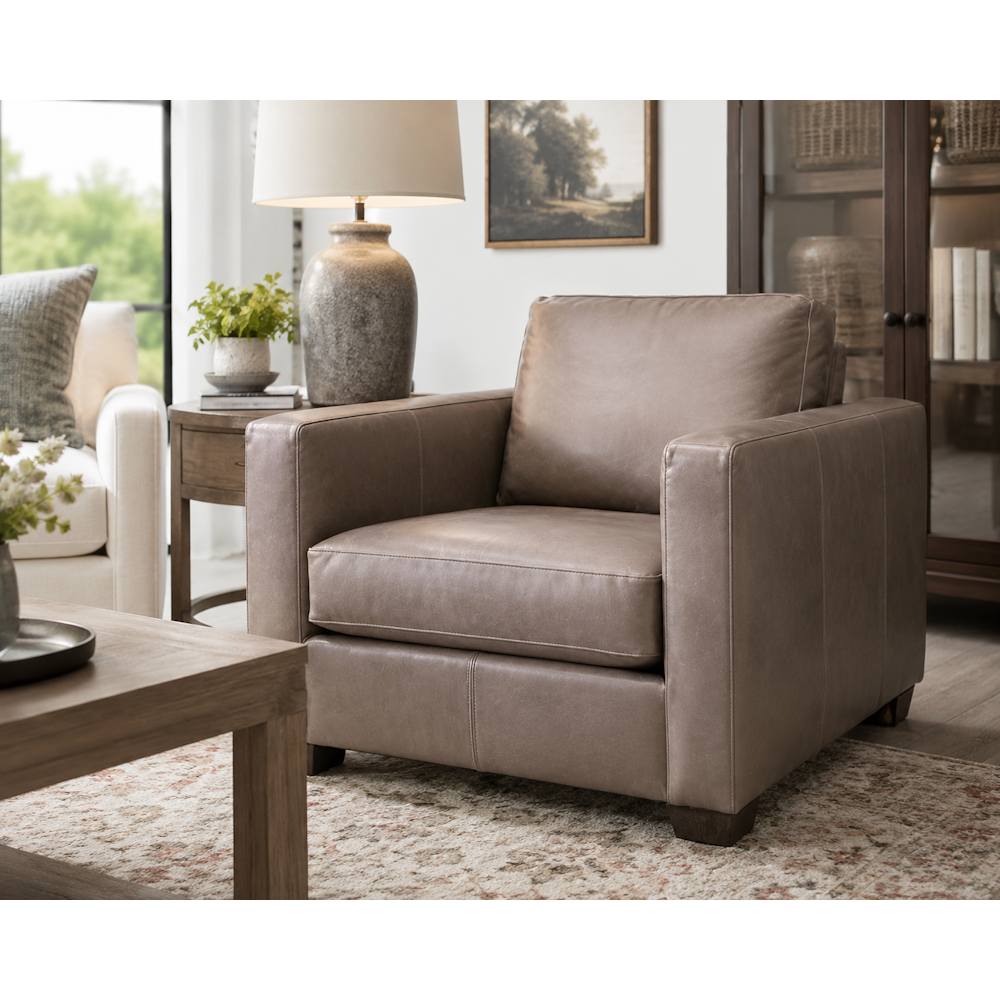 Brown leather armchair in a cozy living room with box arms, loose cushions and dark wood legs.