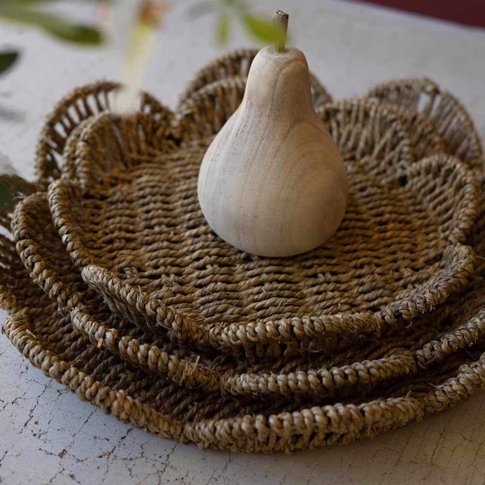 Close-up of stacked, flower-shaped woven seagrass trays topped with a decorative wooden pear.