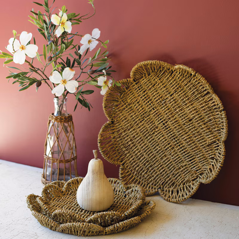Woven seagrass trays styled with a flower vase and wooden pear against a warm terracotta wall.