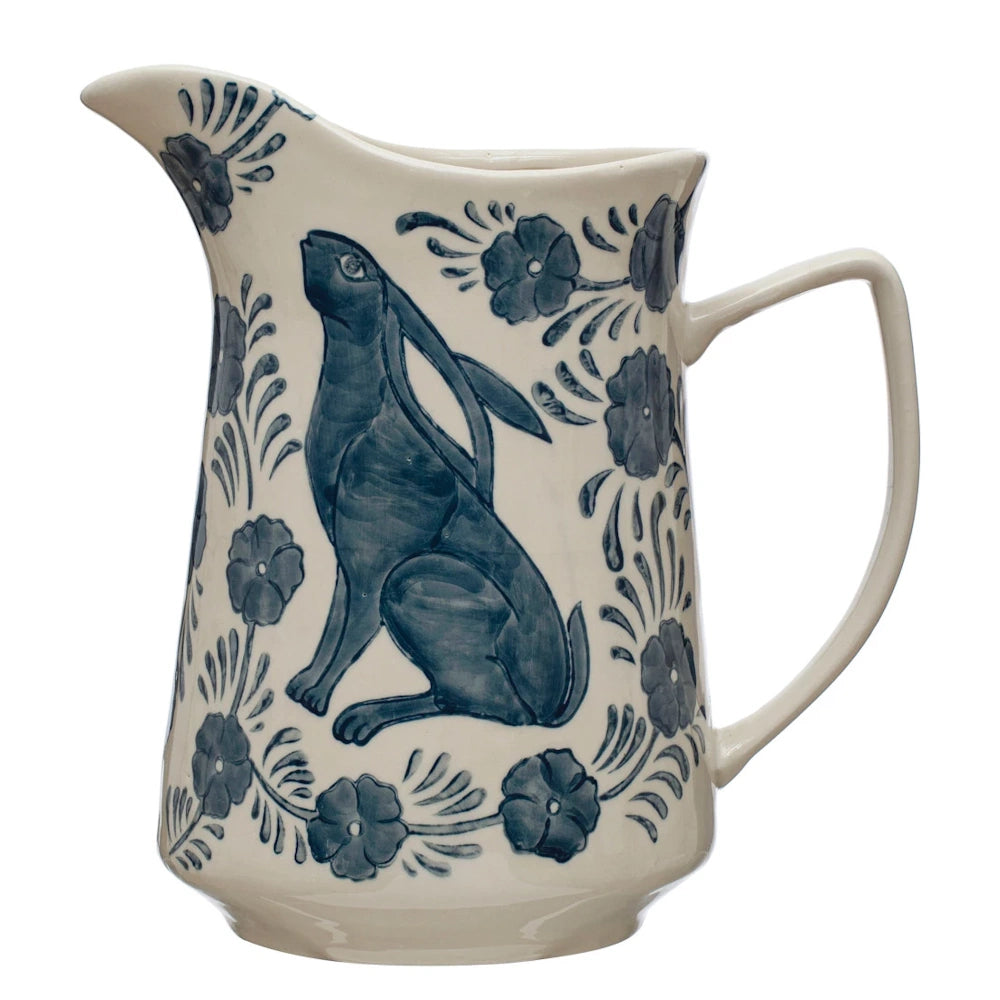 Hand-painted blue and white stoneware pitcher featuring a sitting rabbit and floral motifs on a white background.