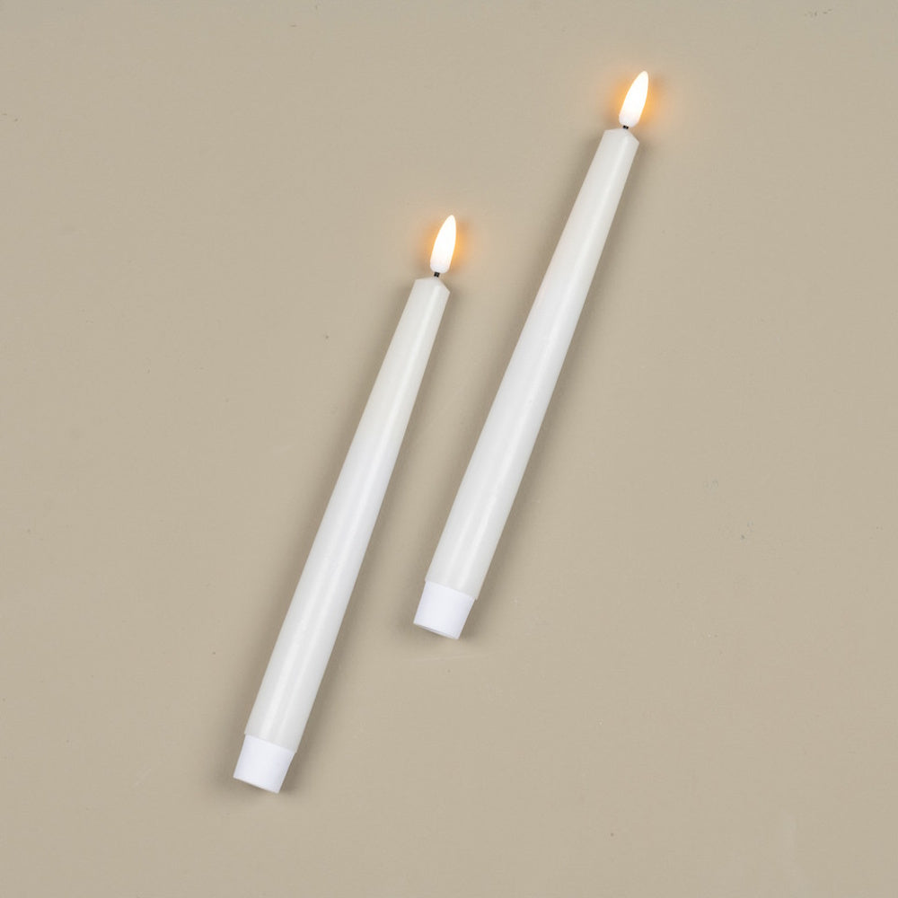 Two white taper candles with glowing flames lying on a beige background.