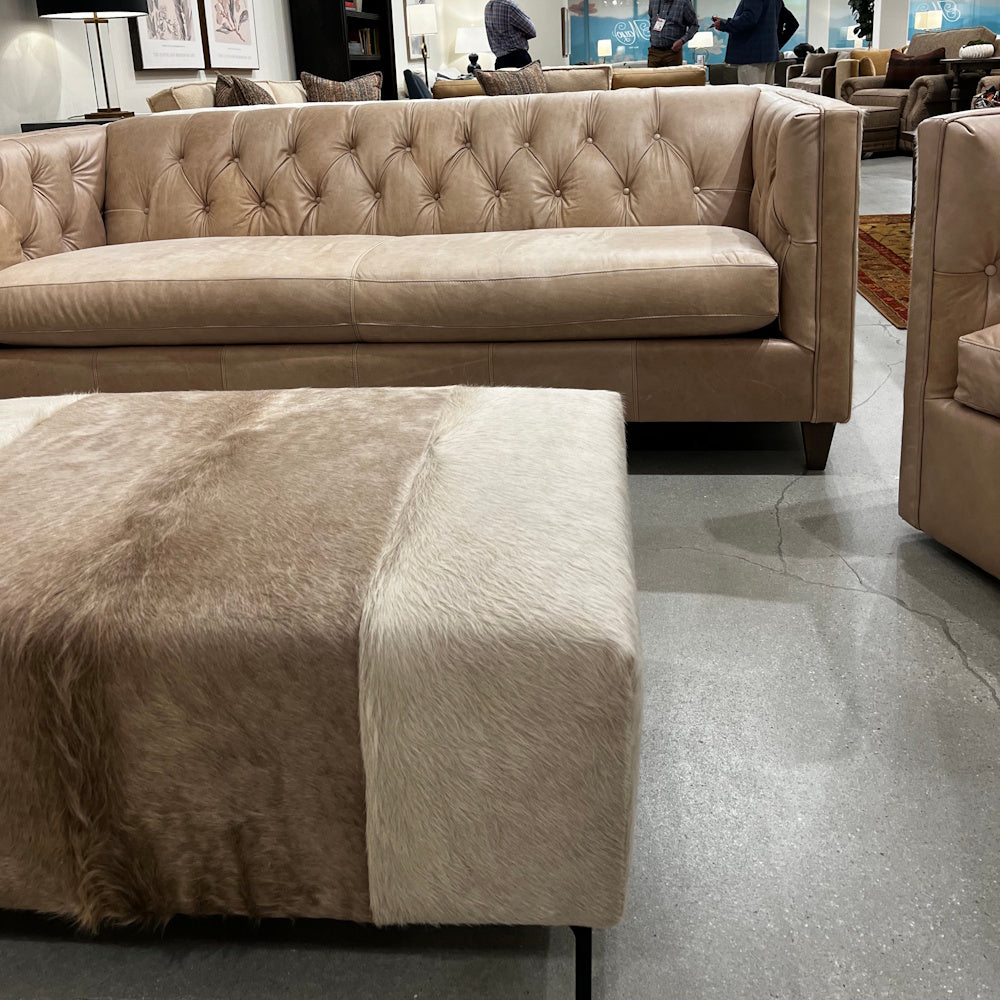 Champagne tufted leather sofa with a cowhide table ottoman in a showroom.