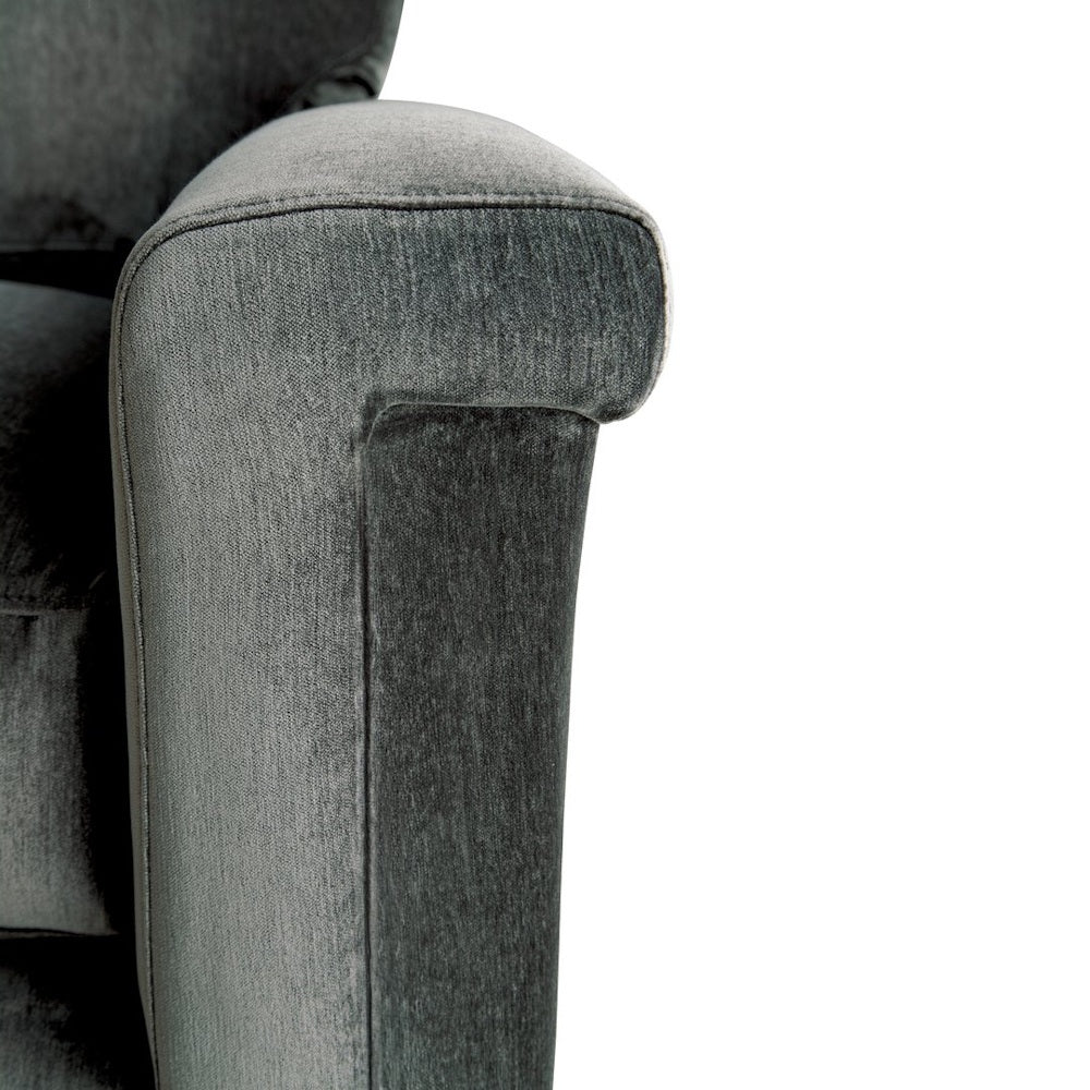 Close-up of a plush dark grey fabric sofa armrest with rolled detailing on a white background.