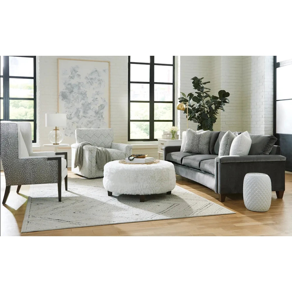 Modern living room with dark grey velvet sofa, white plush ottoman, patterned accent chairs, and area rug.