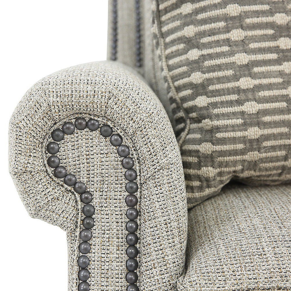Close-up view of a light gray rolled armrest with dark nailhead trim and a patterned throw pillow.
