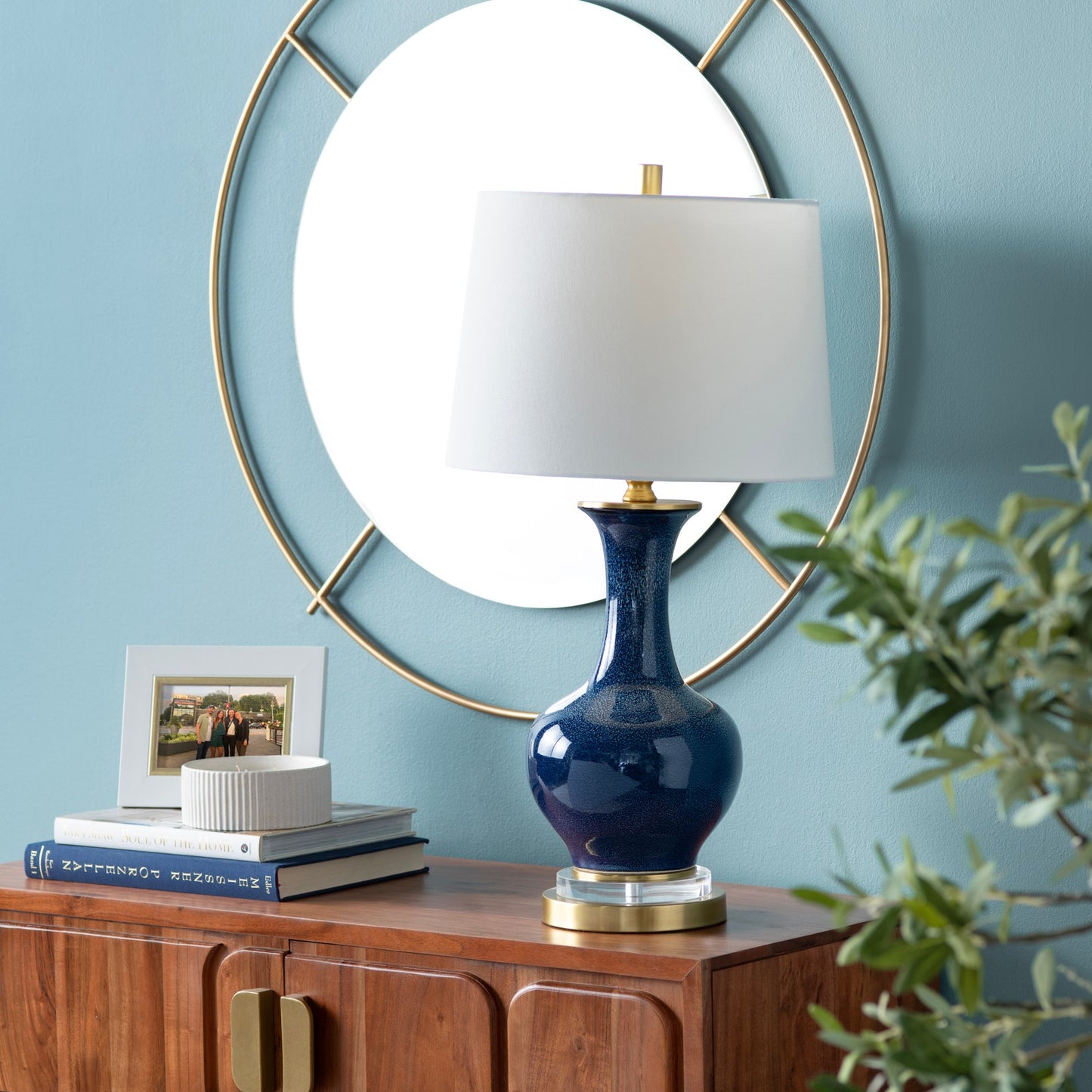 Navy blue lamp with white shade on a wooden console table against a light blue wall.