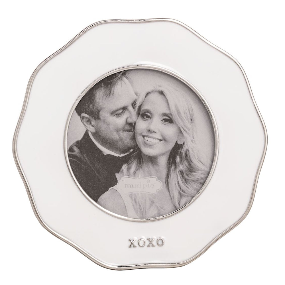 A small, scalloped white enamel picture frame with silver trim and "XOXO" at the bottom, holding a photo of a couple.