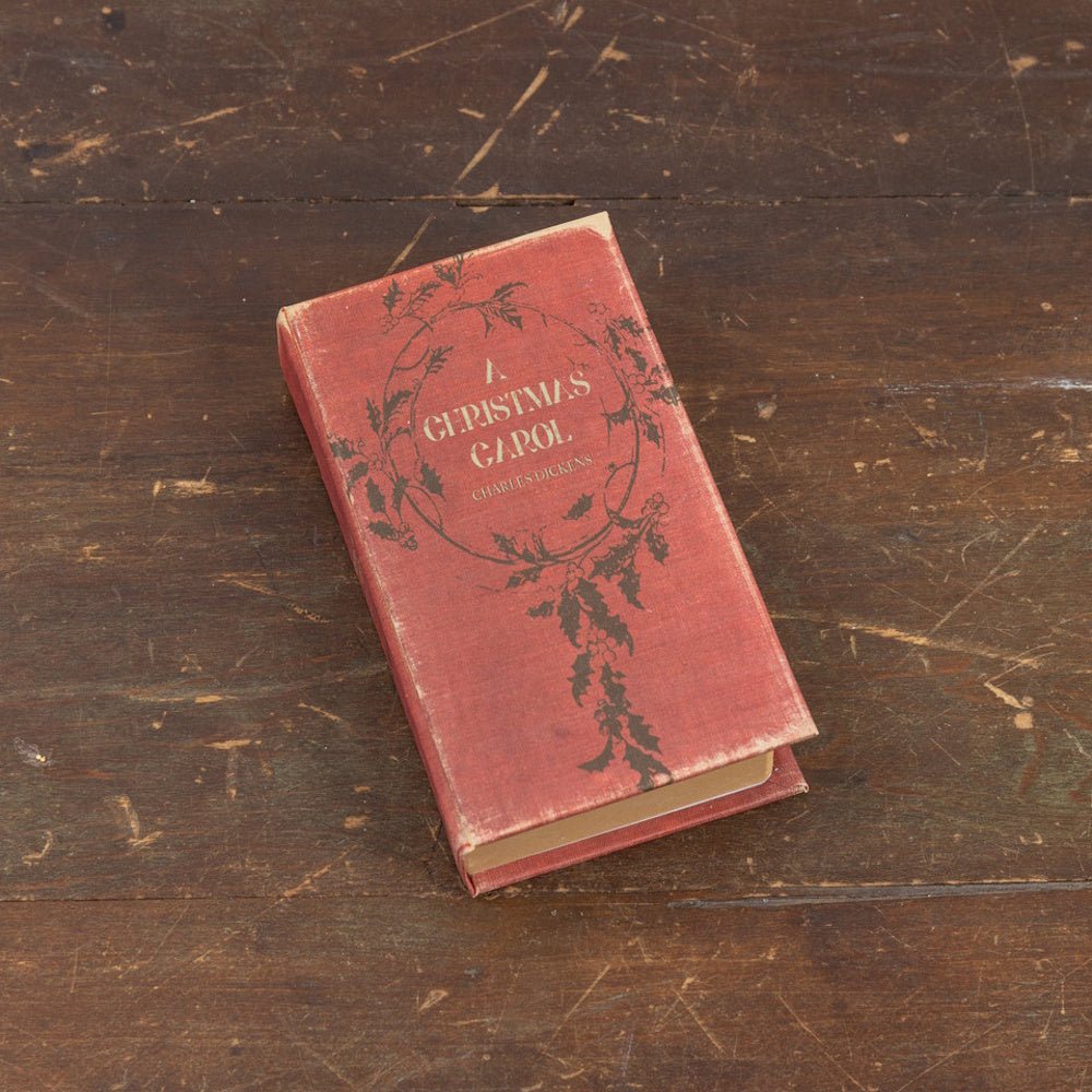 Vintage red book titled "A Christmas Carol" by Charles Dickens resting on a rustic rustic wooden surface.