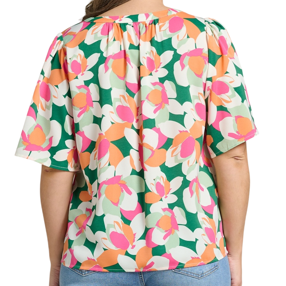Back view of a woman wearing a vibrant, abstract floral print blouse with short flutter sleeves and blue jeans.