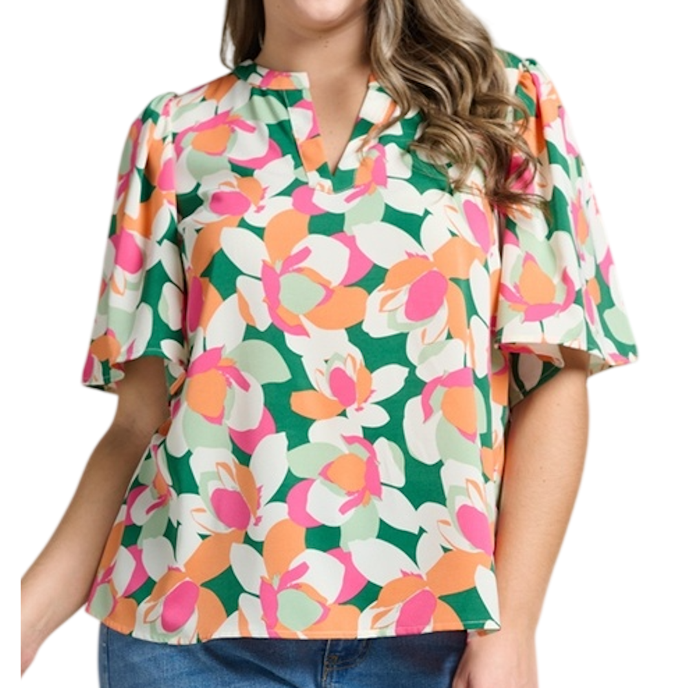 A woman wearing a vibrant, abstract floral print blouse with green, pink, and orange tones and flutter sleeves.