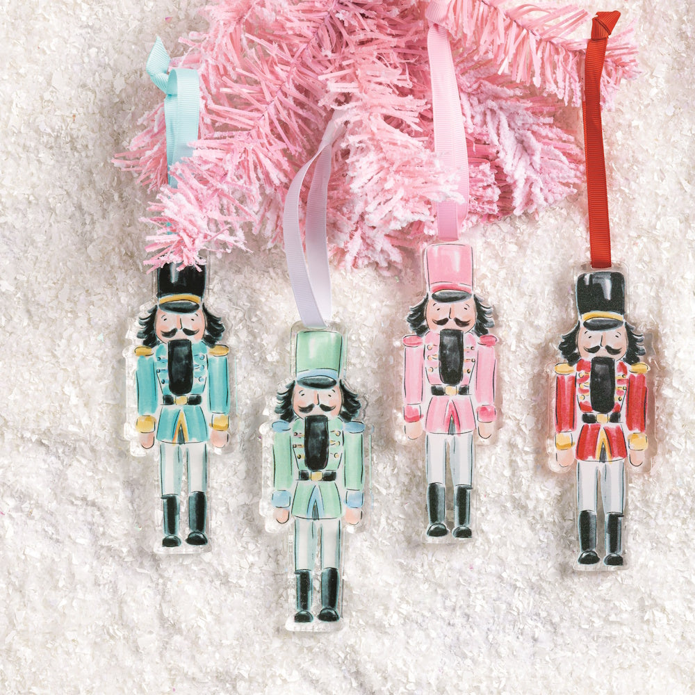 Four acrylic nutcracker ornaments hanging from a pink tinsel tree branch.