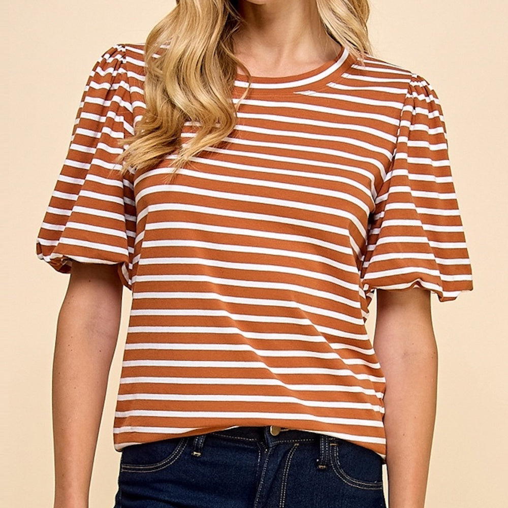 Woman wearing a striped, rust-brown and white t-shirt with puffed short sleeves and dark jeans.