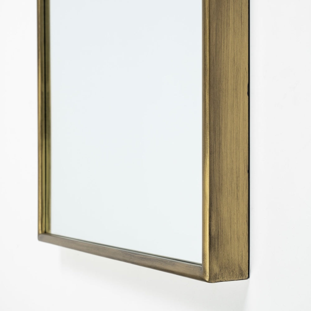 Close-up detail of the bottom corner of a wall mirror with a brushed antique gold metal frame.