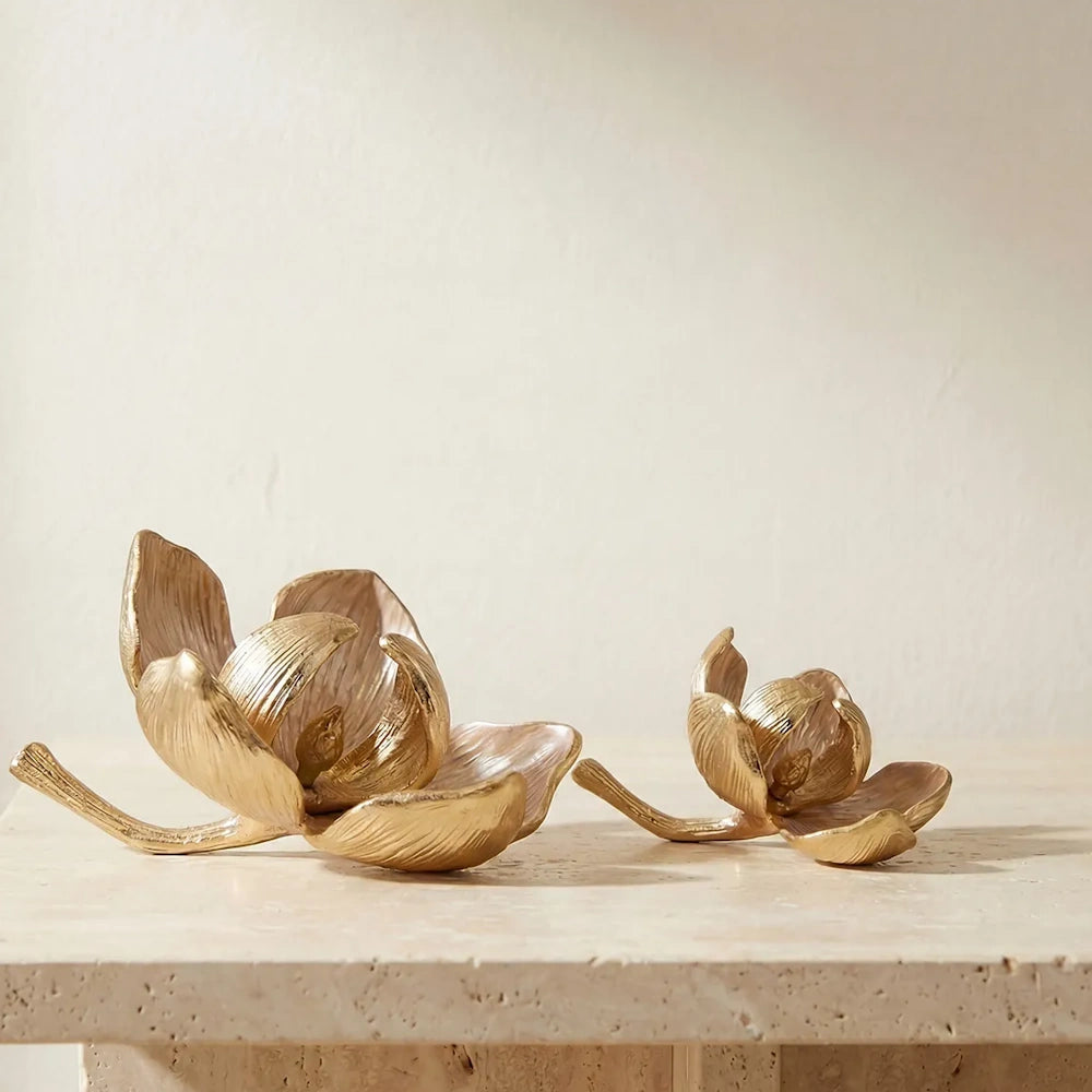 Two gold flower sculptures, one large and one small, rest on a light textured stone surface.