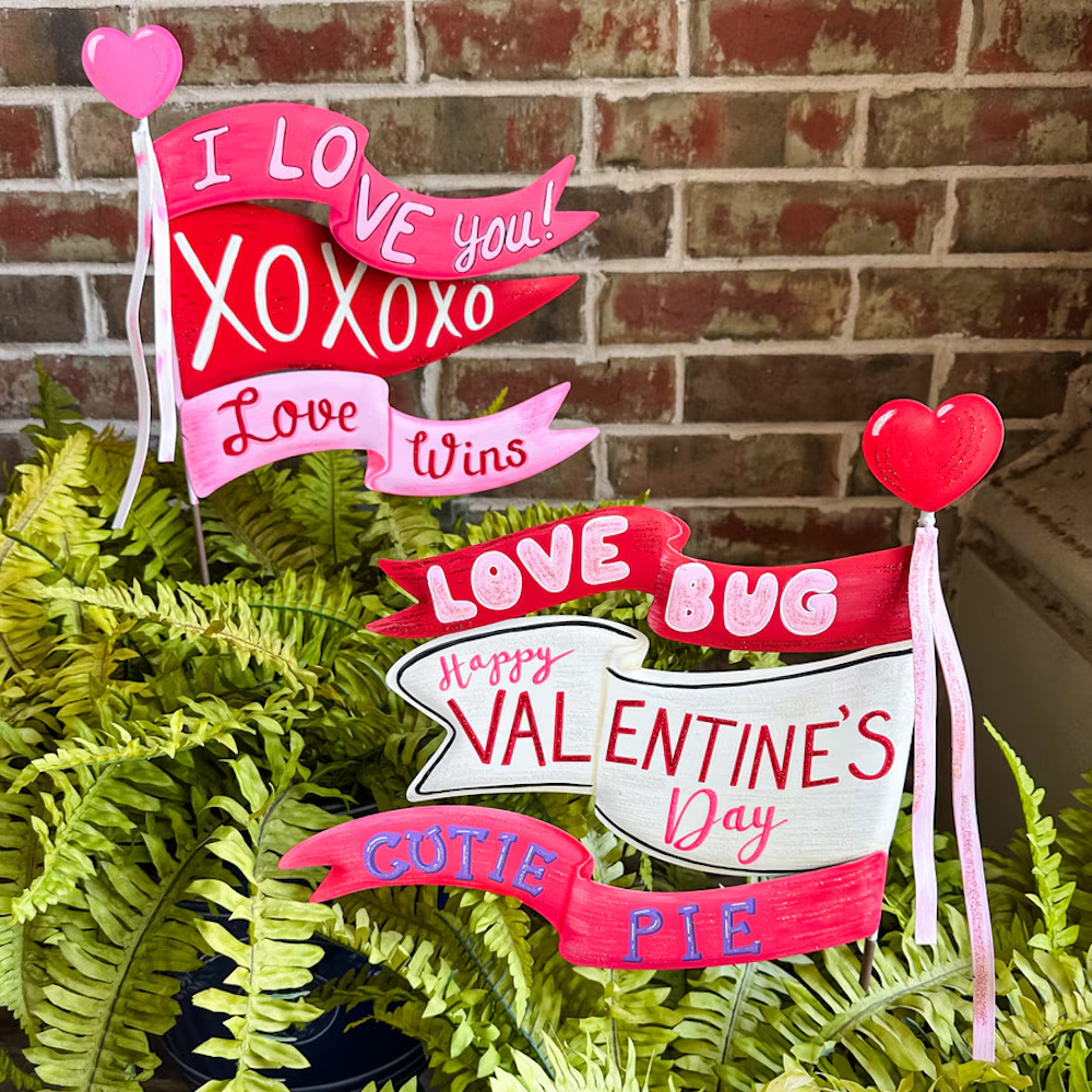 Valentine's Day garden stakes with pink and red banners saying "I Love You" and "Happy Valentine's Day" in ferns.