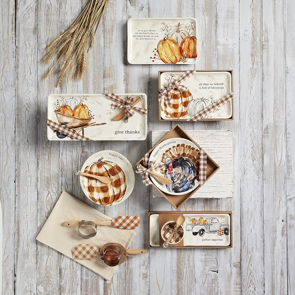 Flat lay of Thanksgiving-themed ceramic serveware and kitchen tools on a white wood surface.