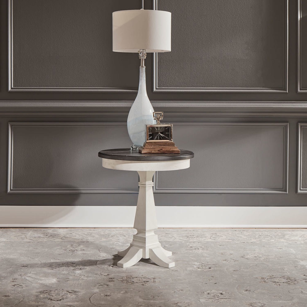 Two-tone pedestal end table styled with a table lamp and vintage clock against a dark wall.