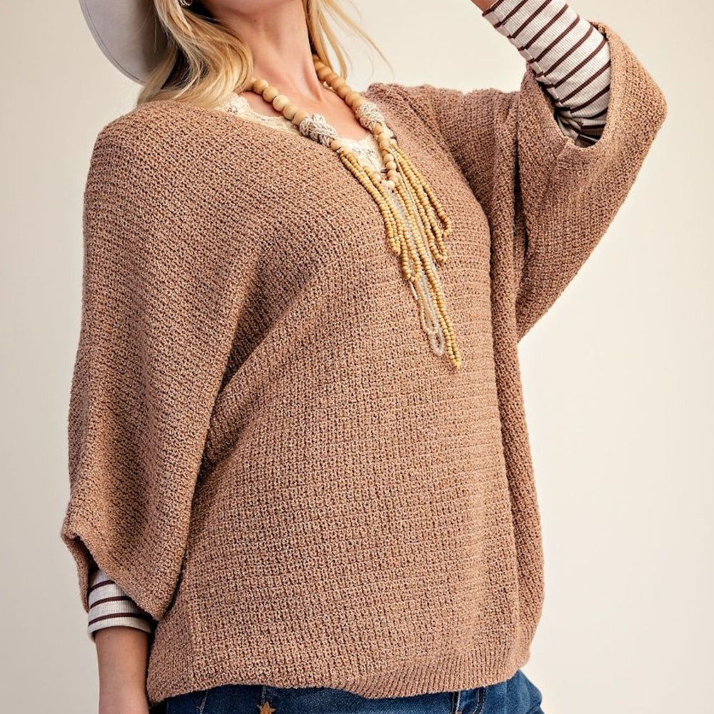 Side view of a woman wearing an almond-colored, loose knit sweater with wide three-quarter length sleeves.