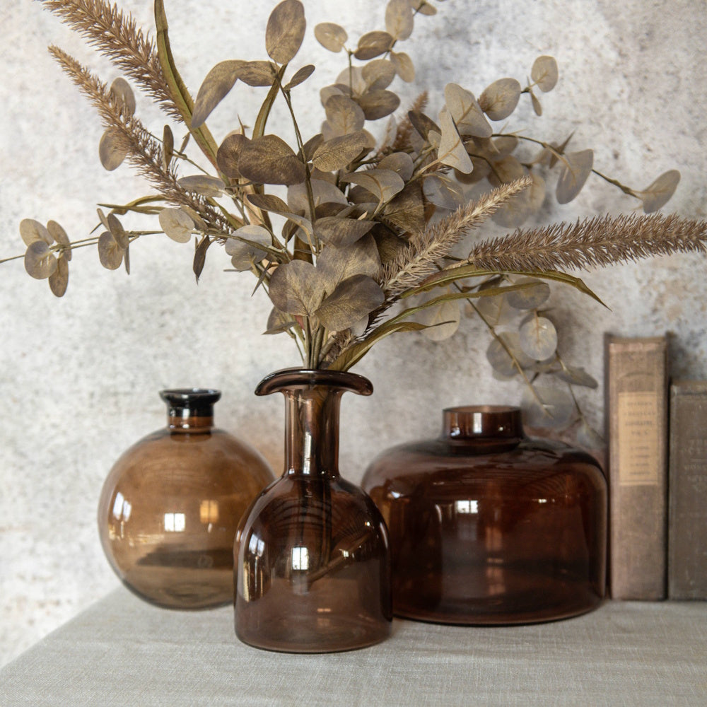 Amber glass vases styled with dried foliage next to vintage books against a textured wall.