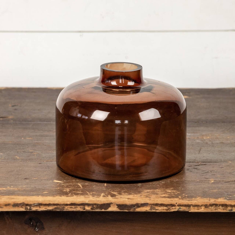 Translucent amber glass vase with a wide, rounded base and a short neck on a rustic wood table.
