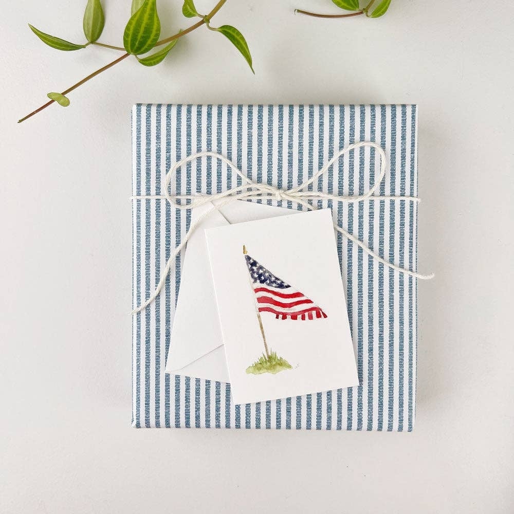 A wrapped gift with blue-and-white stripes, tied with twine and featuring a small American flag notecard.