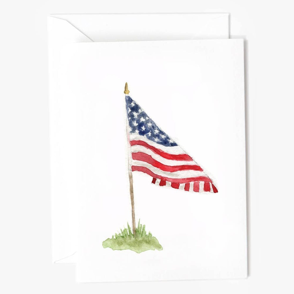 Watercolor painting of the American flag on a flagpole in the grass, featured on a white notecard.