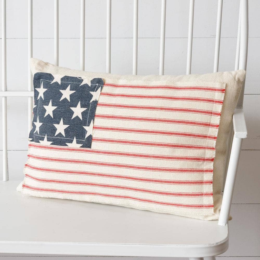 Rectangular throw pillow with an American flag design resting on a white wooden spindle bench.