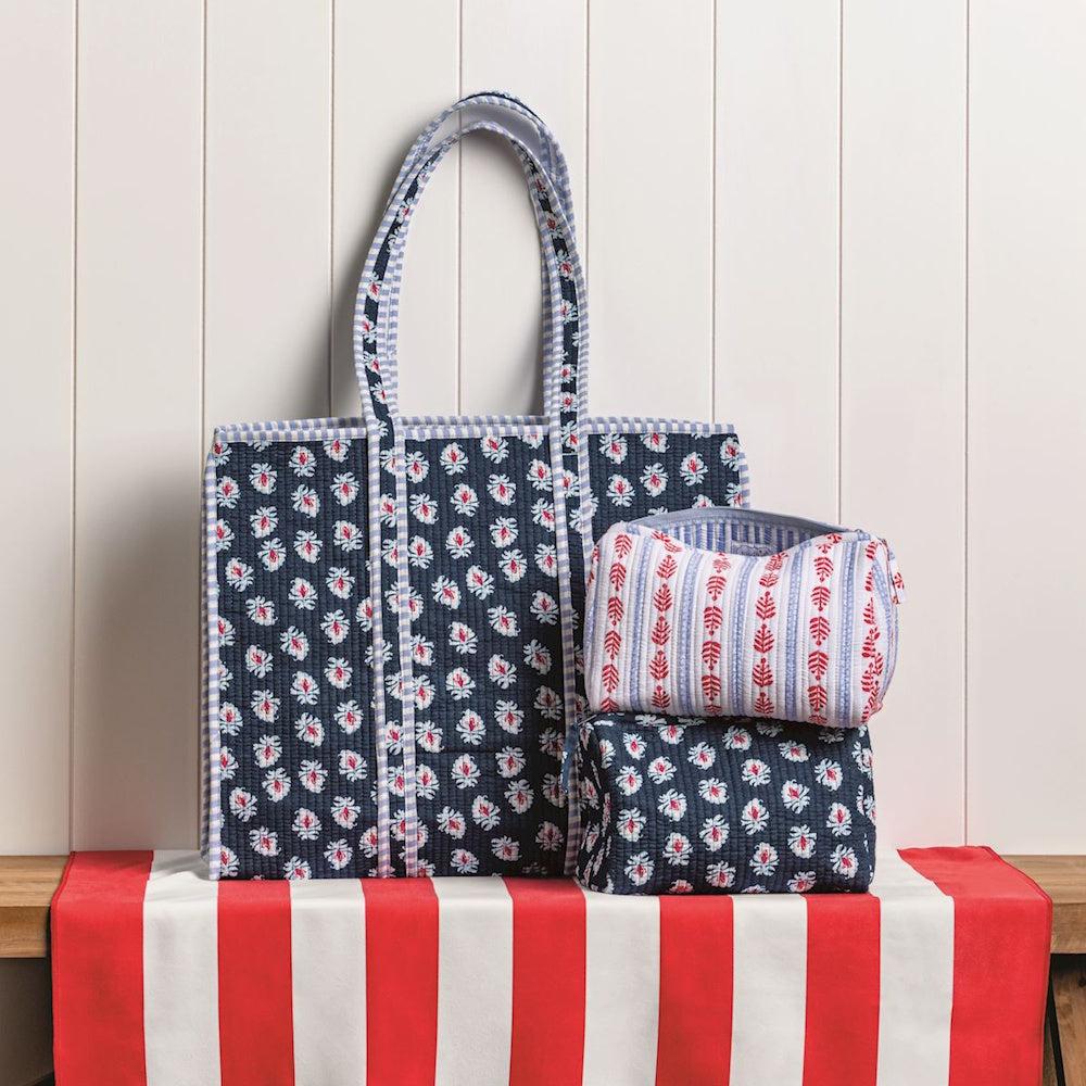 Quilted blue and white block-print tote bag and matching cosmetic pouches on a red striped surface.