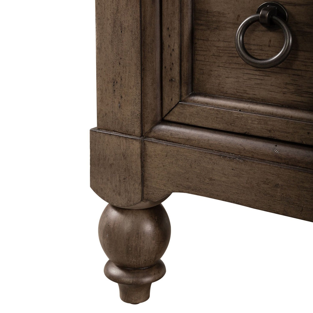 Close-up of a brown wood dresser's turned bun foot, corner detail, and dark metal ring drawer pull.