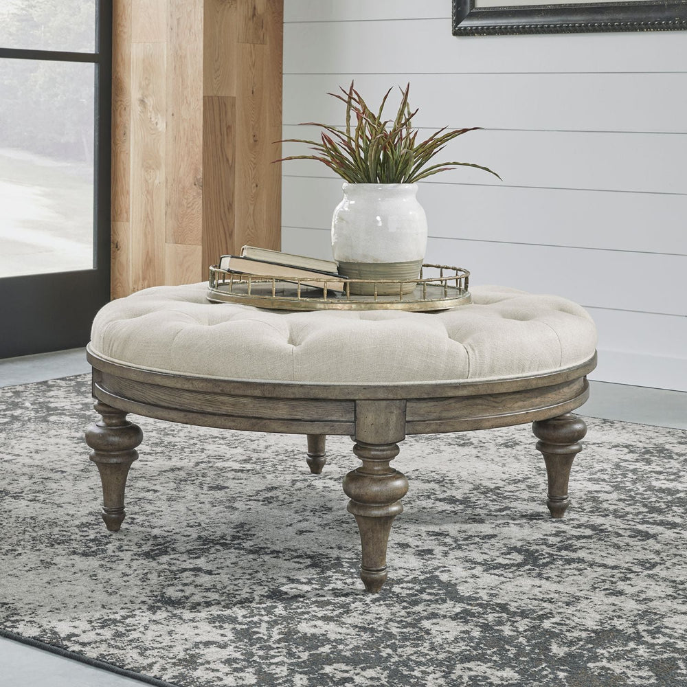 Round tufted cocktail ottoman with a wooden frame and turned legs.