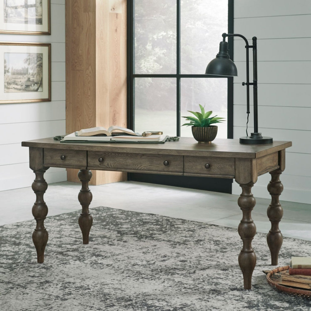 Wooden writing desk styled with a desk lamp, book, and potted plant in a brightly lit room.