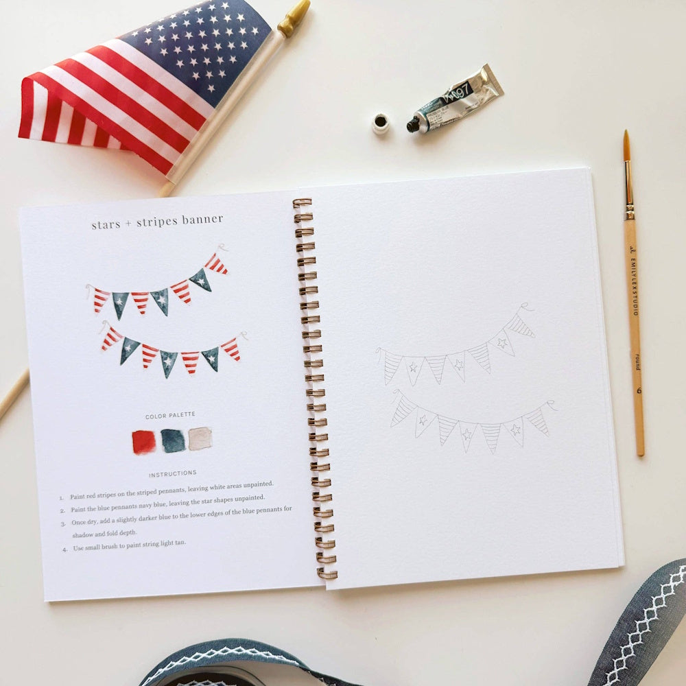 Watercolor Americana stars and stripes banner tutorial in an open workbook with paint, brush, and American flag.