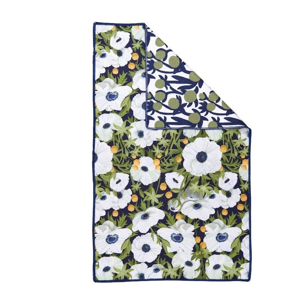 Folded tea towel with white anemone and poppy floral pattern, green leaves, and navy accents on an eco-friendly fabric.