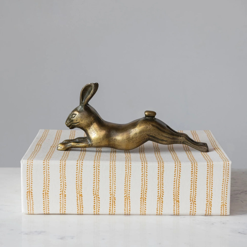 Antique brass rabbit figurine in a leaping pose resting on a striped decorative box.