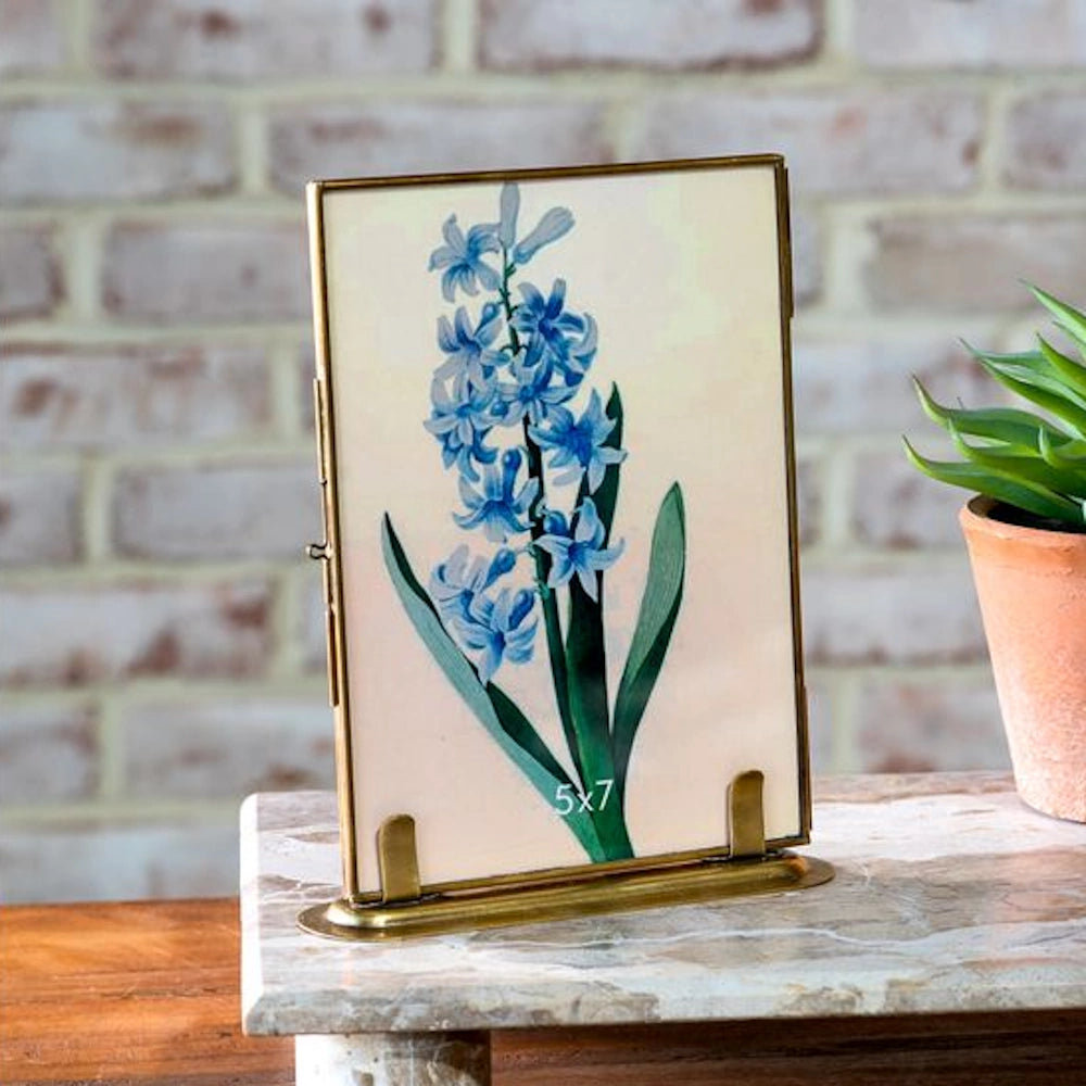 Antique brass 5x7 photo frame with a blue hyacinth botanical print on a marble surface against a brick background.
