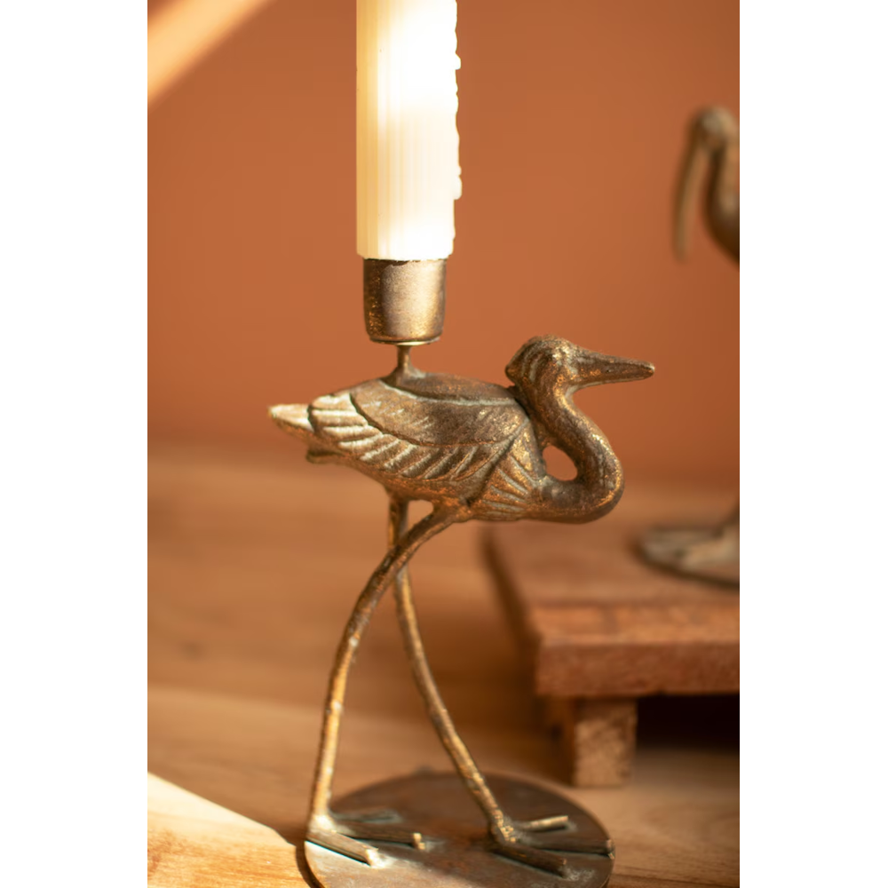Close-up view of a small antique brass shorebird taper candleholder with a white candle.